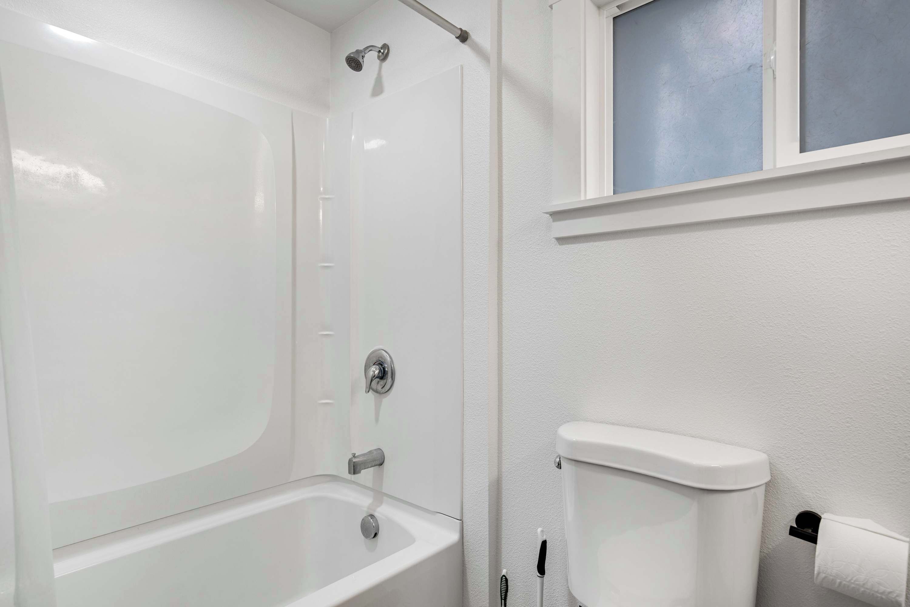 Un baño con bañera, ducha, inodoro y una ventana sobre el inodoro.