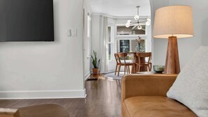 A living room with a sofa, a lamp, a TV, and a dining area with chairs and a table. - Modern 10th St Retreat: Downtown & Hyde Park (Boise)