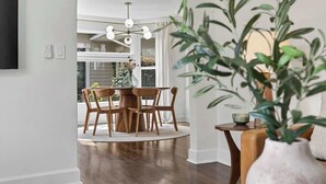 A dining area with a round table and chairs, a vase with greenery, and a view of a house through a window. - Modern 10th St Retreat: Downtown & Hyde Park (Boise)