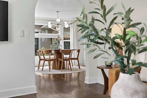 A dining area with a round table and chairs, a vase with greenery, and a view of a house through a window. - Modern 10th St Retreat: Downtown & Hyde Park (Boise)