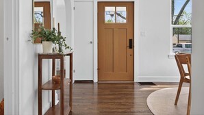 A hallway with a wooden door, a mirror, a potted plant, a wooden chair, and a round rug. - Modern 10th St Retreat: Downtown & Hyde Park (Boise)