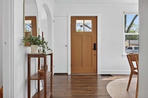 A hallway with a wooden door, a mirror, a potted plant, a wooden chair, and a round rug. - Modern 10th St Retreat: Downtown & Hyde Park (Boise)