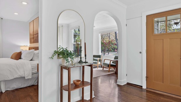 A hotel room with a bed, a wooden console table with a plant, a mirror, and a view of the outside. - Modern 10th St Retreat: Downtown & Hyde Park (Boise)