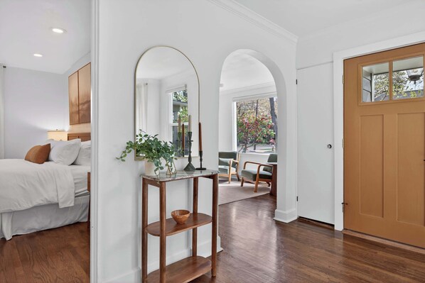 A hotel room with a bed, a wooden console table with a plant, a mirror, and a view of the outside. - Modern 10th St Retreat: Downtown & Hyde Park (Boise)
