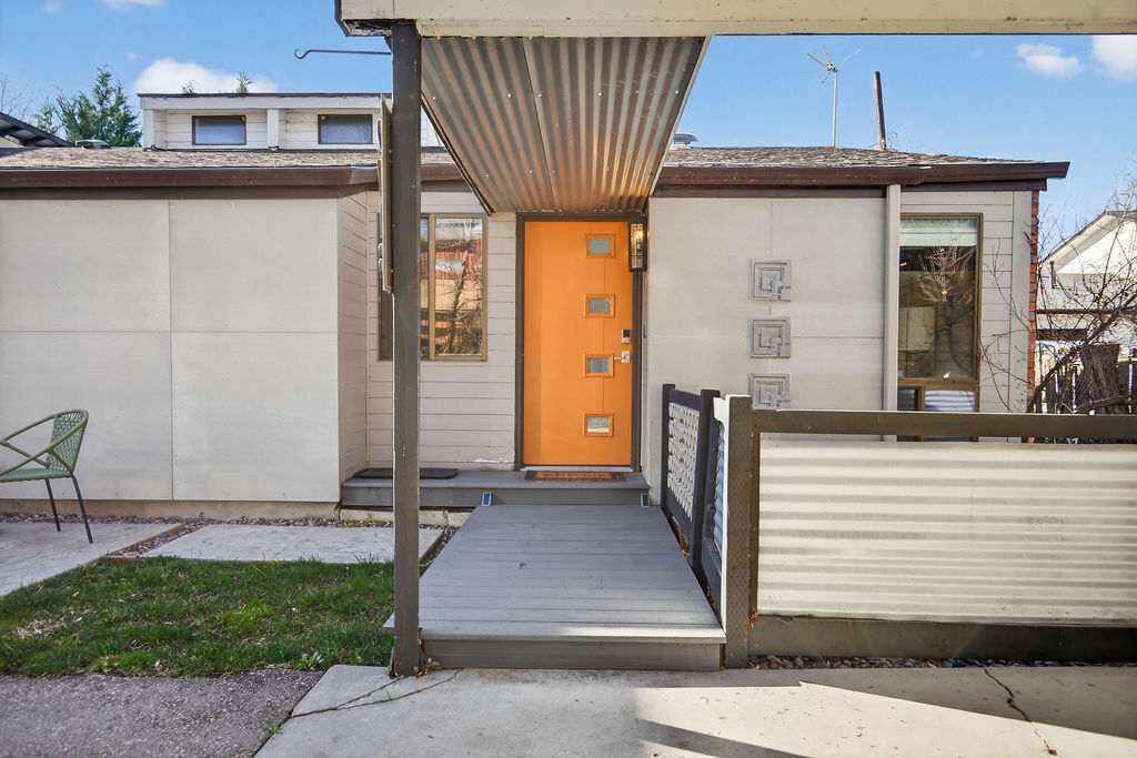 Un edificio con techo plano, terraza de madera y portón metálico.