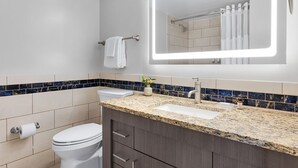 A modern bathroom with a toilet, sink, vanity, and a large mirror with integrated lighting. - CRYSTAL SHORES MARRIOTT exclusive!! (Marco Island)