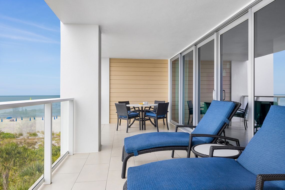 A balcony with wicker lounge chairs, a table with chairs, and a view of the beach.