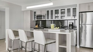 A modern kitchen with white cabinets, stainless steel appliances, and a bar area with white chairs. - CRYSTAL SHORES MARRIOTT exclusive!! (Marco Island)
