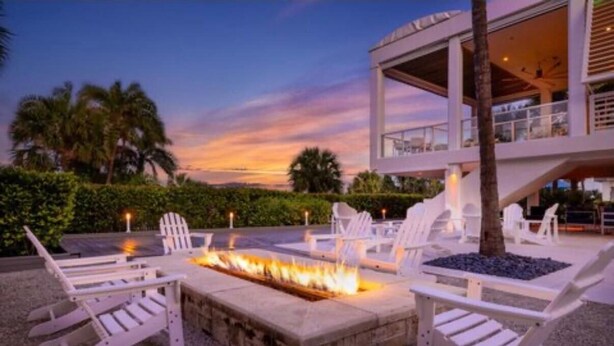 A modern outdoor seating area with Adirondack chairs and a fire pit, surrounded by a pool and palm trees. - CRYSTAL SHORES MARRIOTT exclusive!! (Marco Island)