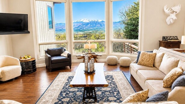 A living room with a large window, a flat-screen TV, a sofa, a coffee table, and a decorative lamp. - Ultimate AFA Graduation Estate: 5 Private Acres - 5 Mins to North Gate (Colorado Springs)