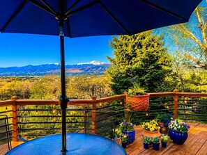 Una terraza con vistas a las montañas, un paraguas azul y plantas en macetas.