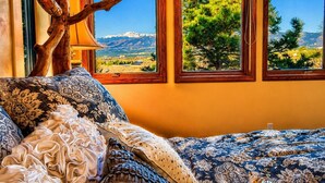 A bed with patterned bedding, a wooden branch above a window, and a mountain view. - Ultimate AFA Graduation Estate: 5 Private Acres - 5 Mins to North Gate (Colorado Springs)