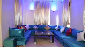Ein Zimmer mit blauem Sofagarnitur, einem Couchtisch in der Mitte und Vorhängen.