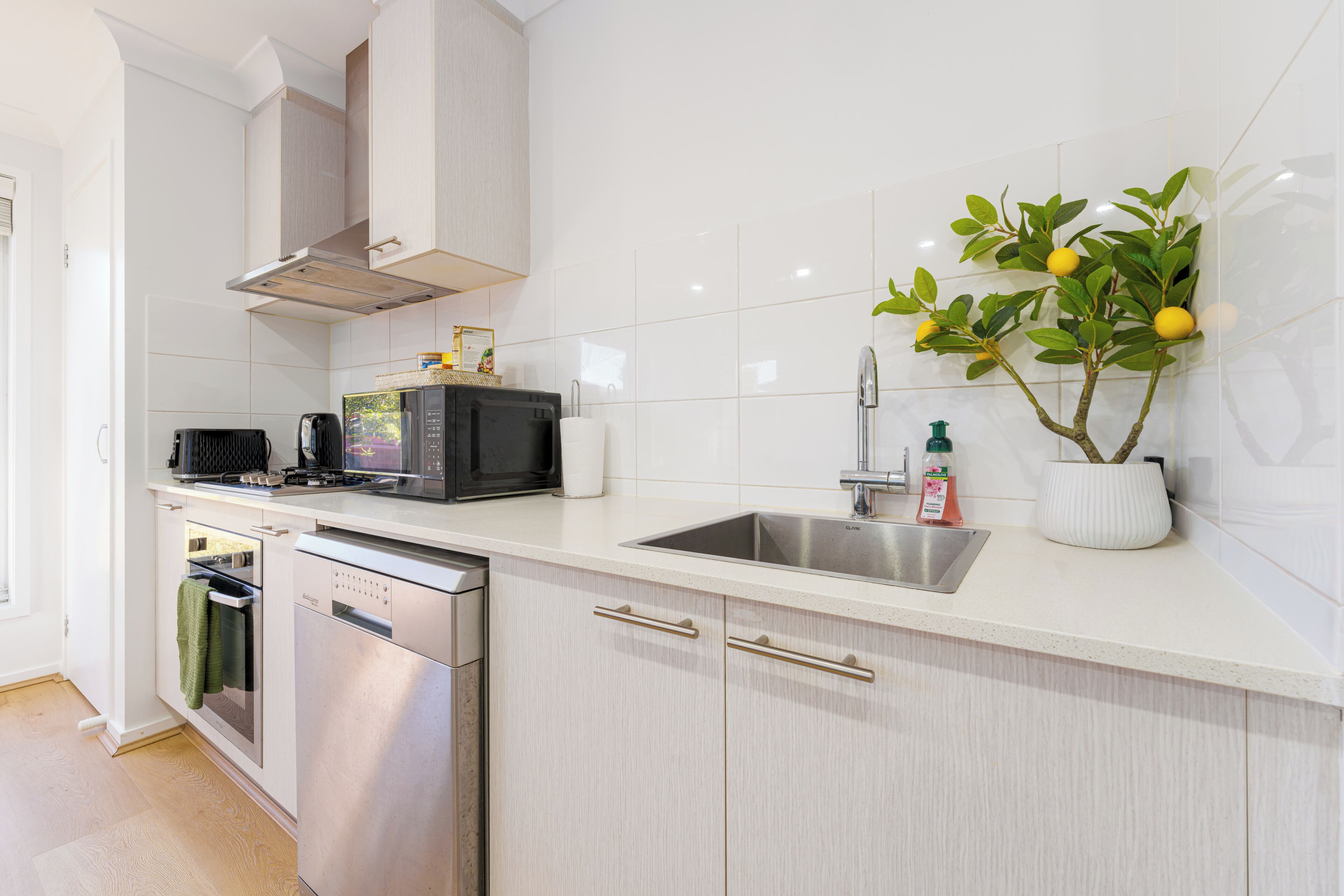 A modern kitchen with stainless steel appliances, a white tiled backsplash, and a potted plant.