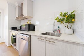A modern kitchen with stainless steel appliances, a white tiled backsplash, and a potted plant.