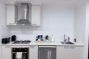 Eine moderne Küche mit weißen Schränken, einer Edelstahl-Dunstabzugshaube, einem Geschirrspüler und einem Spülbecken.