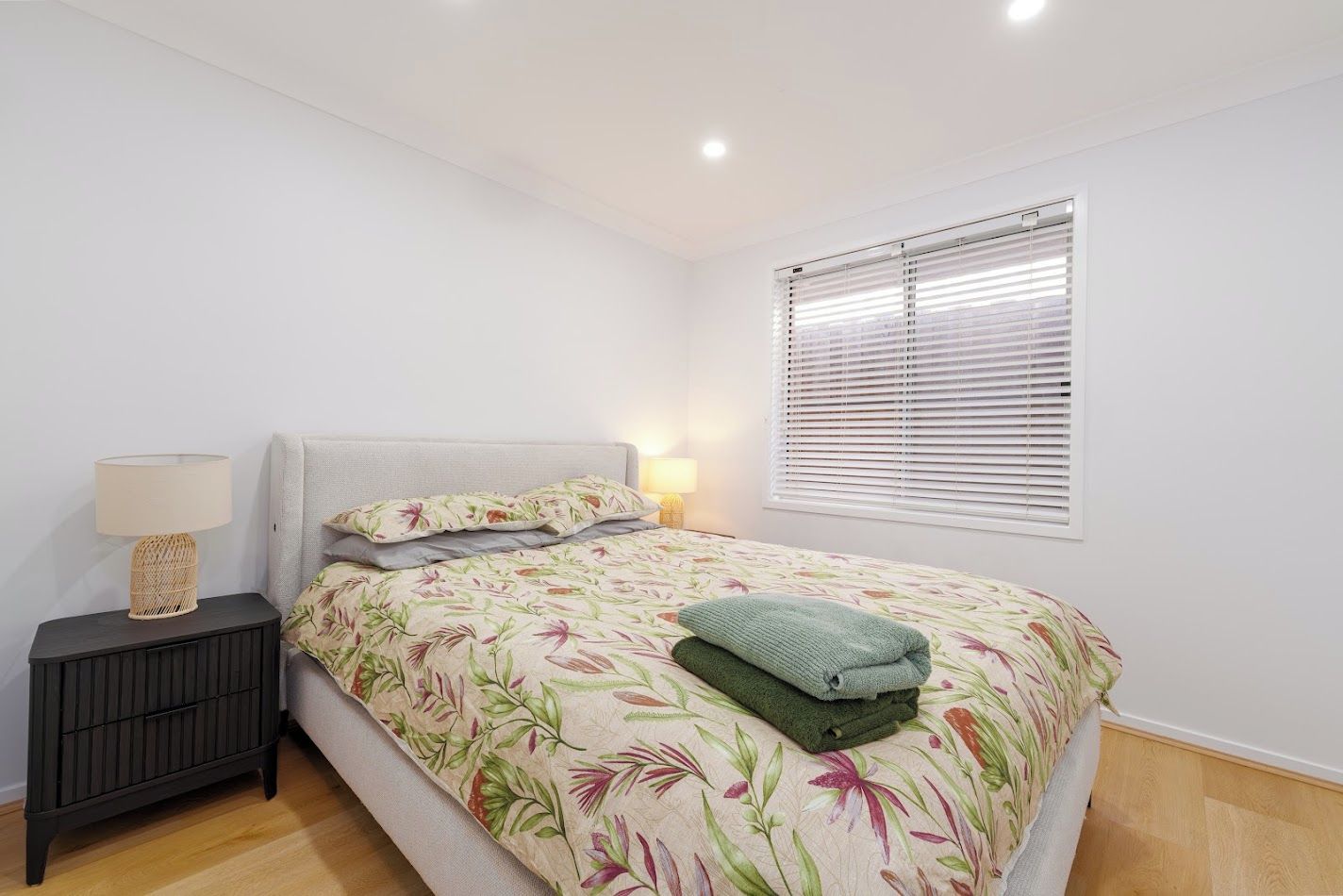 A bedroom with a bed, a nightstand, a lamp, and a window with blinds.