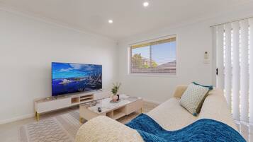 A modern living room with a flat-screen TV, a sofa, a coffee table, and a window with blinds.