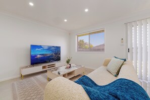 Een moderne woonkamer met een flatscreen televisie, een bank, een salontafel en een raam met zonwering.