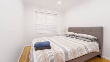 Un dormitorio con cama, mesita de noche, lámpara y ventana con persianas.