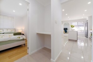 A modern bedroom with a bed, bedside table, and a view into the living area.