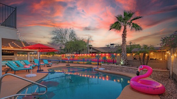 A swimming pool with lounge chairs, a flamingo float, and a sunset sky. - Peoria Resort! Spacious 7BR, Heated Pool, Theater, Hot Tub, Ping Pong & More! (Peoria)