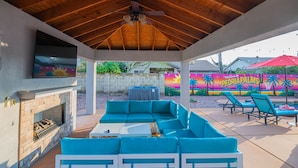 A covered outdoor patio with a stone fireplace, a sectional sofa, and a ceiling fan. - Peoria Resort! Spacious 7BR, Heated Pool, Theater, Hot Tub, Ping Pong & More! (Peoria)