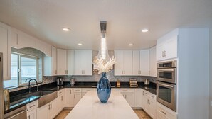 A modern kitchen with white cabinets, a central island, stainless steel appliances, and a decorative vase. - Peoria Resort! Spacious 7BR, Heated Pool, Theater, Hot Tub, Ping Pong & More! (Peoria)