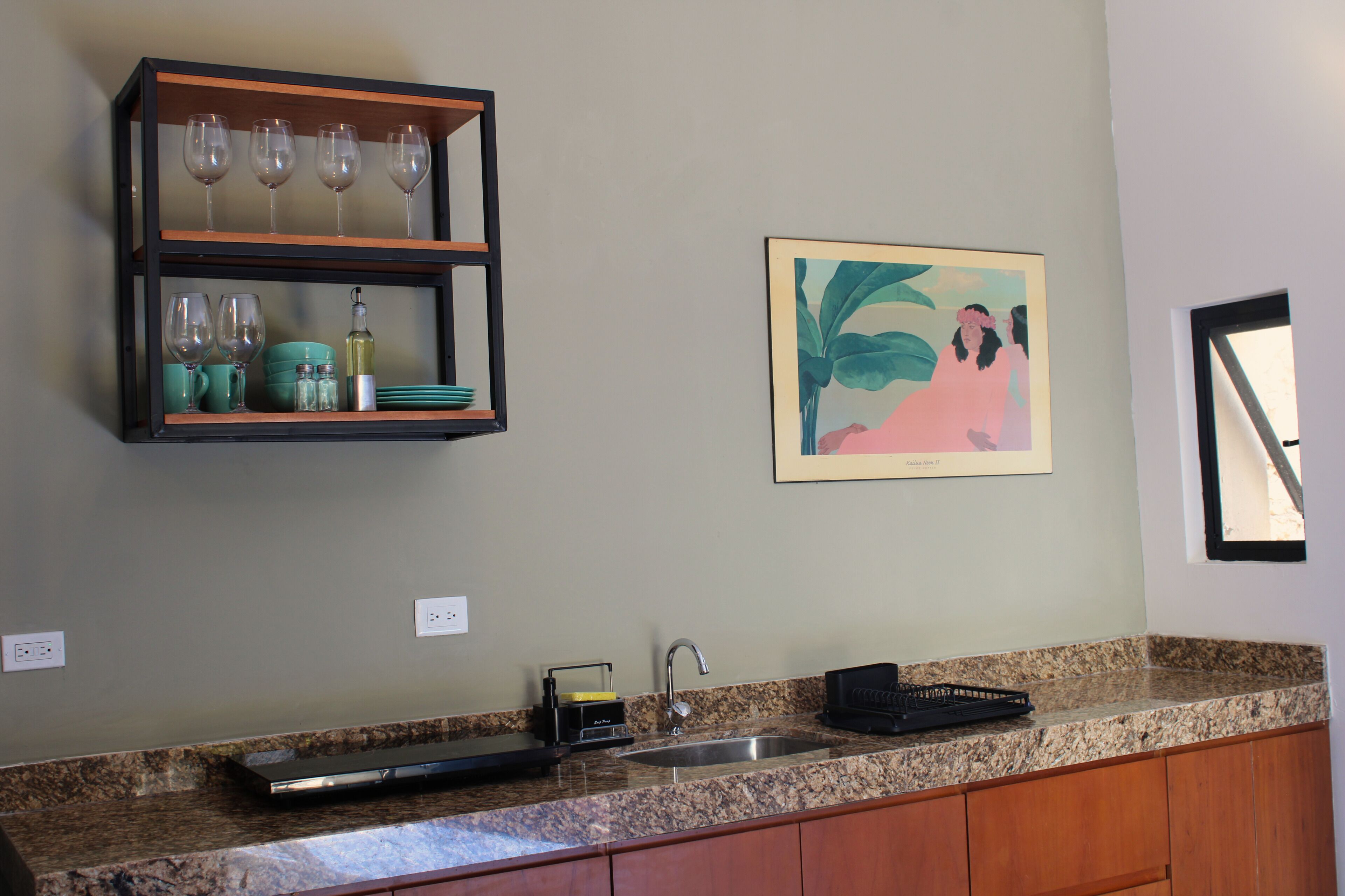 Una cucina con un piano di lavoro in granito, una dispensa integrata con bicchieri da vino, un lavandino e un quadro incorniciato appeso al muro.