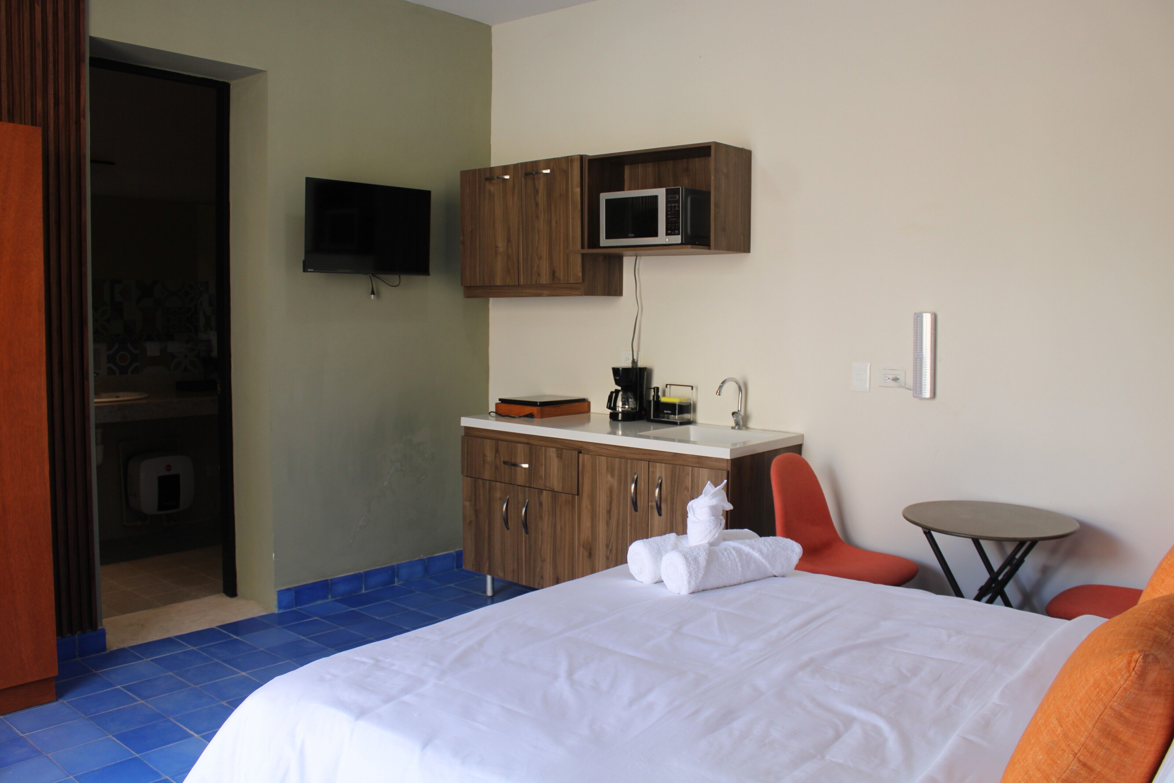 A hotel room with a bed, a small table, a microwave, and a TV mounted on the wall.