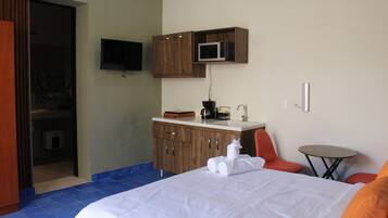 A hotel room with a bed, a small table, a microwave, and a TV mounted on the wall.