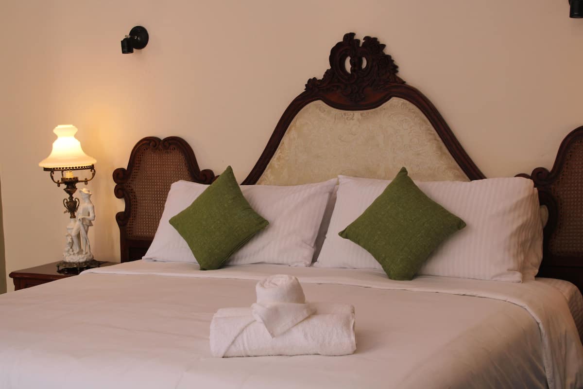 Una cama bien hecha con sábanas blancas, dos almohadas verdes y una toalla doblada sobre la cama.