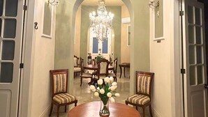 A grand hallway with a large chandelier, a round table with a vase of flowers, and a dining area with chairs and a table. - Casa Ku'x (Merida)