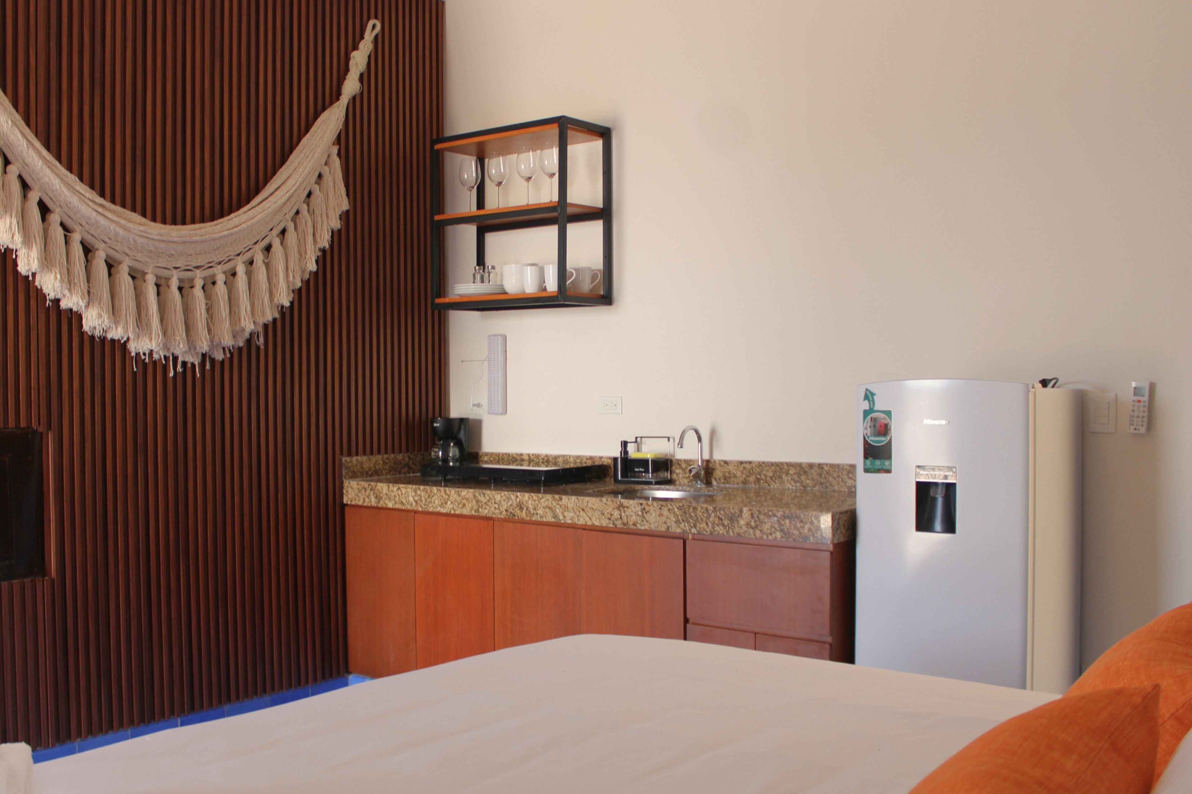 Habitación de hotel con cama, un armario de madera, una zona de cocina con lavamanos y un refrigerador.