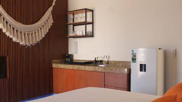 Habitación de hotel con cama, un armario de madera, una zona de cocina con lavamanos y un refrigerador.