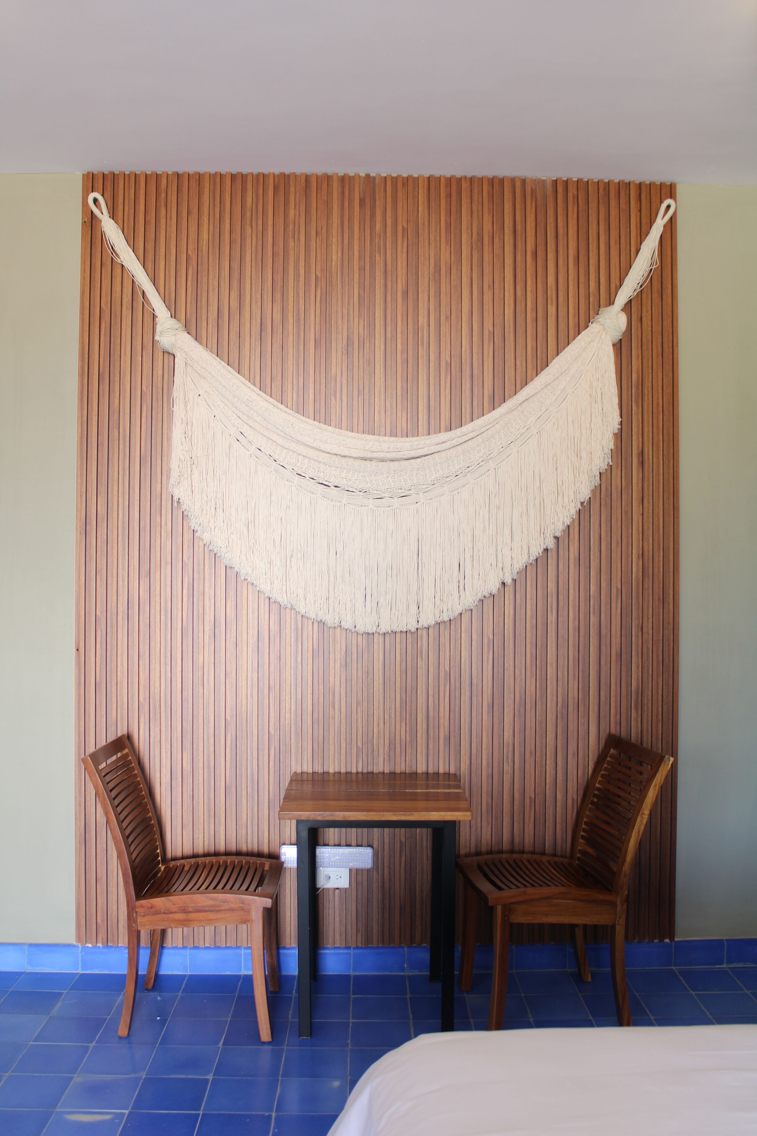 A room with a wooden slat wall, a hammock, two wooden chairs, and a small table.