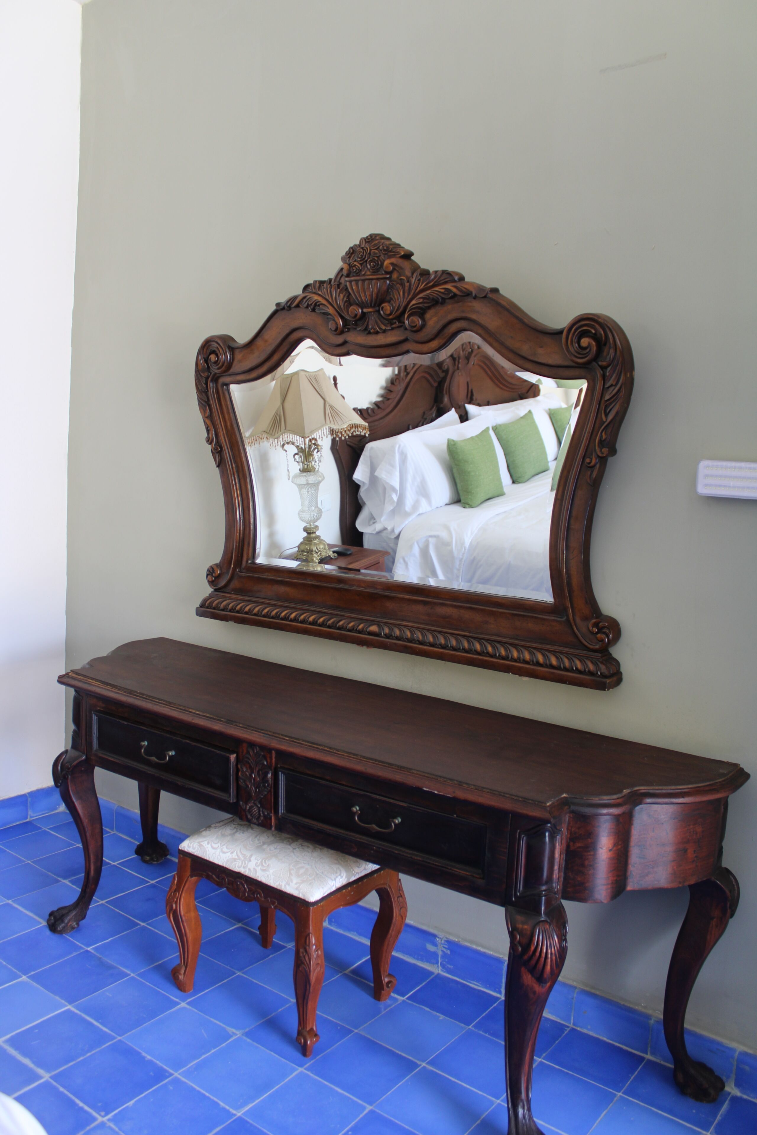 A wooden dresser with a mirror above it, reflecting a bed with pillows.