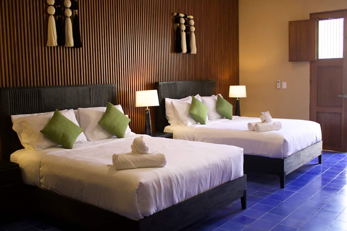 Dos camas dobles con sábanas blancas y almohadas verdes, paneles de madera en las paredes y suelo de baldosas azules.