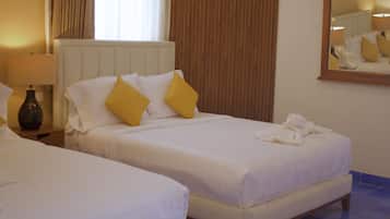 Two single beds with white linens and yellow pillows, a bedside lamp, and a mirror on the wall.