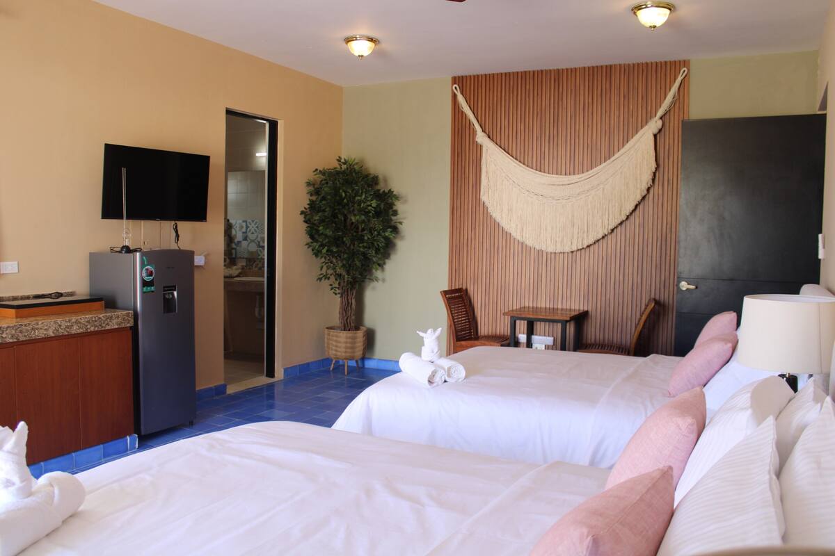 Habitación de hotel con dos camas, televisión, minibar, planta y una hamaca.