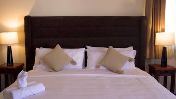 A neatly made bed with white linens and two beige pillows, flanked by two bedside tables with lamps.