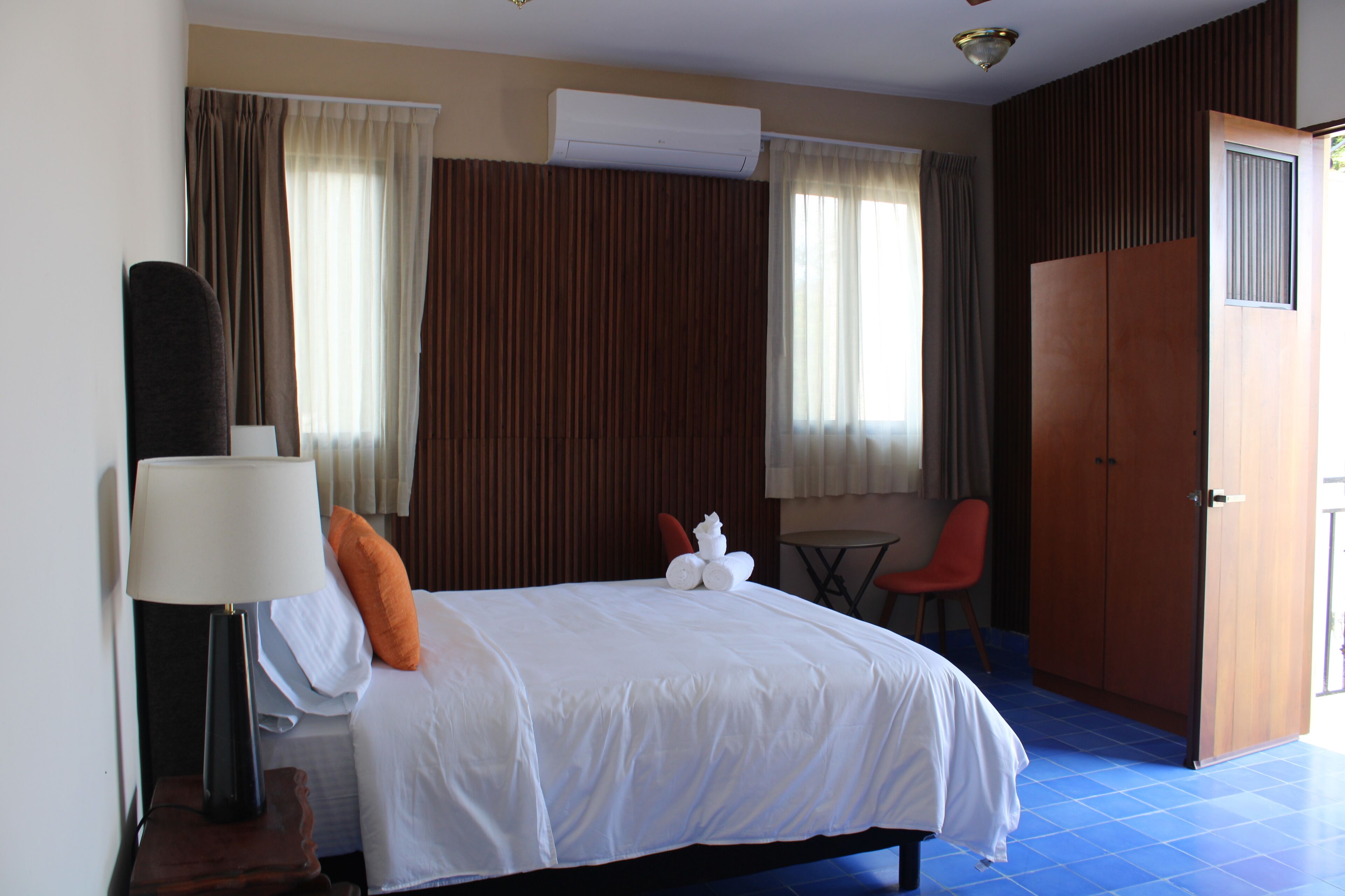 A hotel room with a bed, a desk, a chair, an air conditioning unit, and a wardrobe.