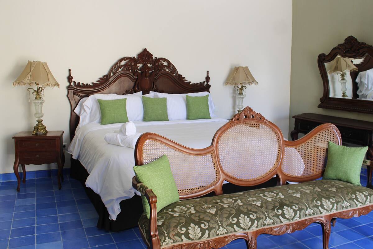 Habitación de hotel con una cama grande, dos mesitas de noche, un banco de madera y un espejo.