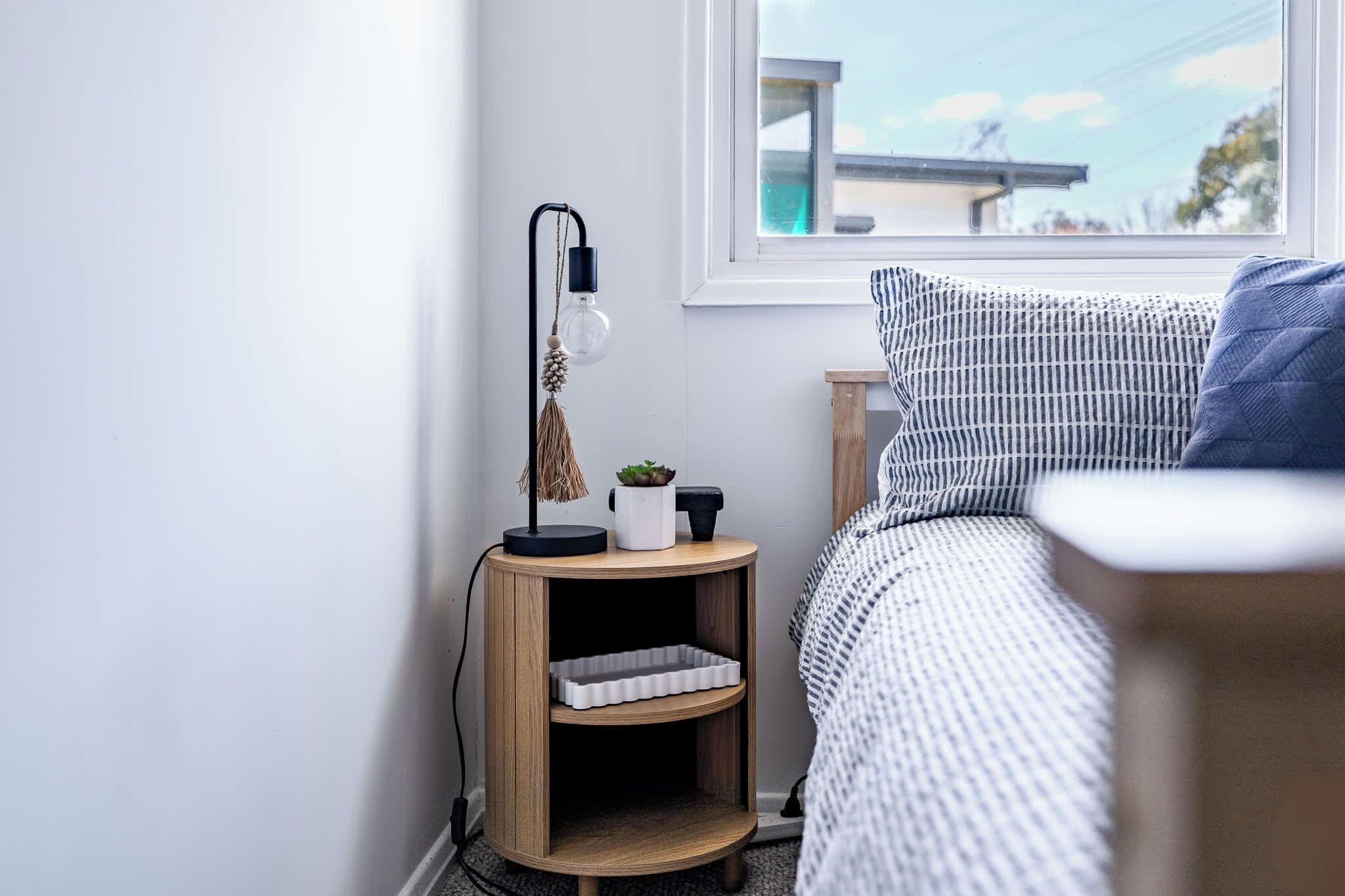 Ein Schlafzimmer mit einem Bett, einem Nachttisch, einer Lampe und einem Fenster.