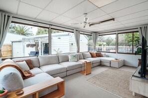 A spacious living room with a sectional sofa, a wooden coffee table, and a ceiling fan. - Classic 70's renovated Luxury Shack Pet Friendly (Ocean Grove)