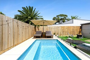 A rectangular swimming pool with a wooden fence, two lounge chairs, and a canopy. - Classic 70's Luxury Shack | Pet Friendly (Ocean Grove)