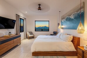 A bedroom with a bed, a TV, a window with a mountain view, a chair, and a painting. - Modern Desert Beach Retreat, Rincon del Afan (Palmilla)