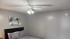 Un dormitorio con una cama, un ventilador de techo, una lámpara de pared y un cuadro.