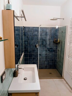A bathroom with a white sink, a shower with a glass door, and dark blue tiles. - Incantevole vista mare - Mareri apartments (Sanremo)