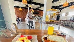 A breakfast table with fruit and toast, a buffet area in the background, and a fan on the ceiling.
